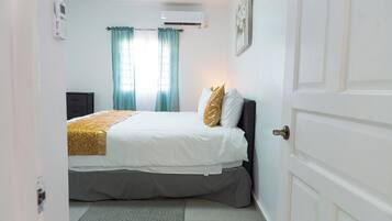 Une chambre à coucher comprenant un lit, une table de chevet, un climatiseur fixé au mur et une porte.