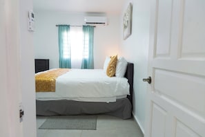 Ein Schlafzimmer mit einem Bett, einem Nachttisch, einer Wand-Klimaanlage und einer Tür.