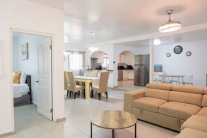 A modern living room with a sofa, a round wooden coffee table, and a dining area with chairs and a table. - Novels Villa is a family-friendly home with the Caribbean Sea as your backyard. (Grand-Case)