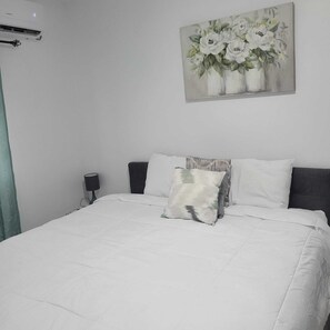 Un dormitorio con cama, mesita de noche, lámpara y un cuadro de flores en la pared.