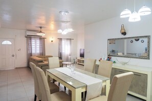 A modern living room with a dining area, featuring a sofa, a dining table with chairs, a TV, and a large mirror. - Novels Villa is a family-friendly home with the Caribbean Sea as your backyard. (Grand-Case)