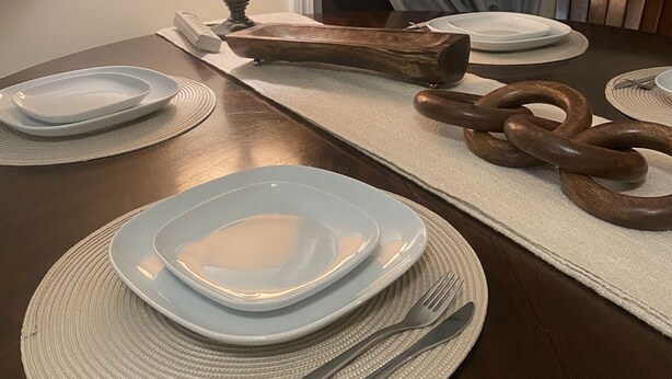 Een eettafel gedekt met borden, bestek en een decoratieve houten schakel.