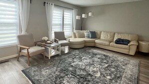 Ein Wohnzimmer mit einem beigefarbenen Sofa, einem runden Couchtisch, einem Sessel und einem großen Teppich.