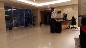 Una moderna hall d'albergo con una reception, un addetto alla sicurezza e un receptionist.
