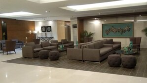 Un'ampia hall con diverse zone relax, tra cui divani e poltrone, disposte attorno a un tavolino da caffè. Sono presenti piante in vaso e opere d'arte alle pareti.