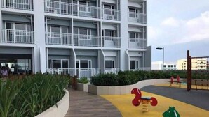 Un edificio a più piani con balconi, un'area giochi con attrezzature colorate e una zona verde con piante.