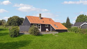 Une maison avec un toit en pente, une cheminée et un petit porche doté d’un banc.