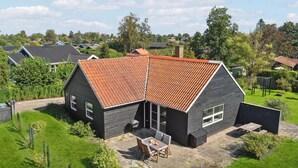 Une maison moderne avec un toit en pente, une terrasse dotée de mobilier d’extérieur et un jardin bien entretenu.