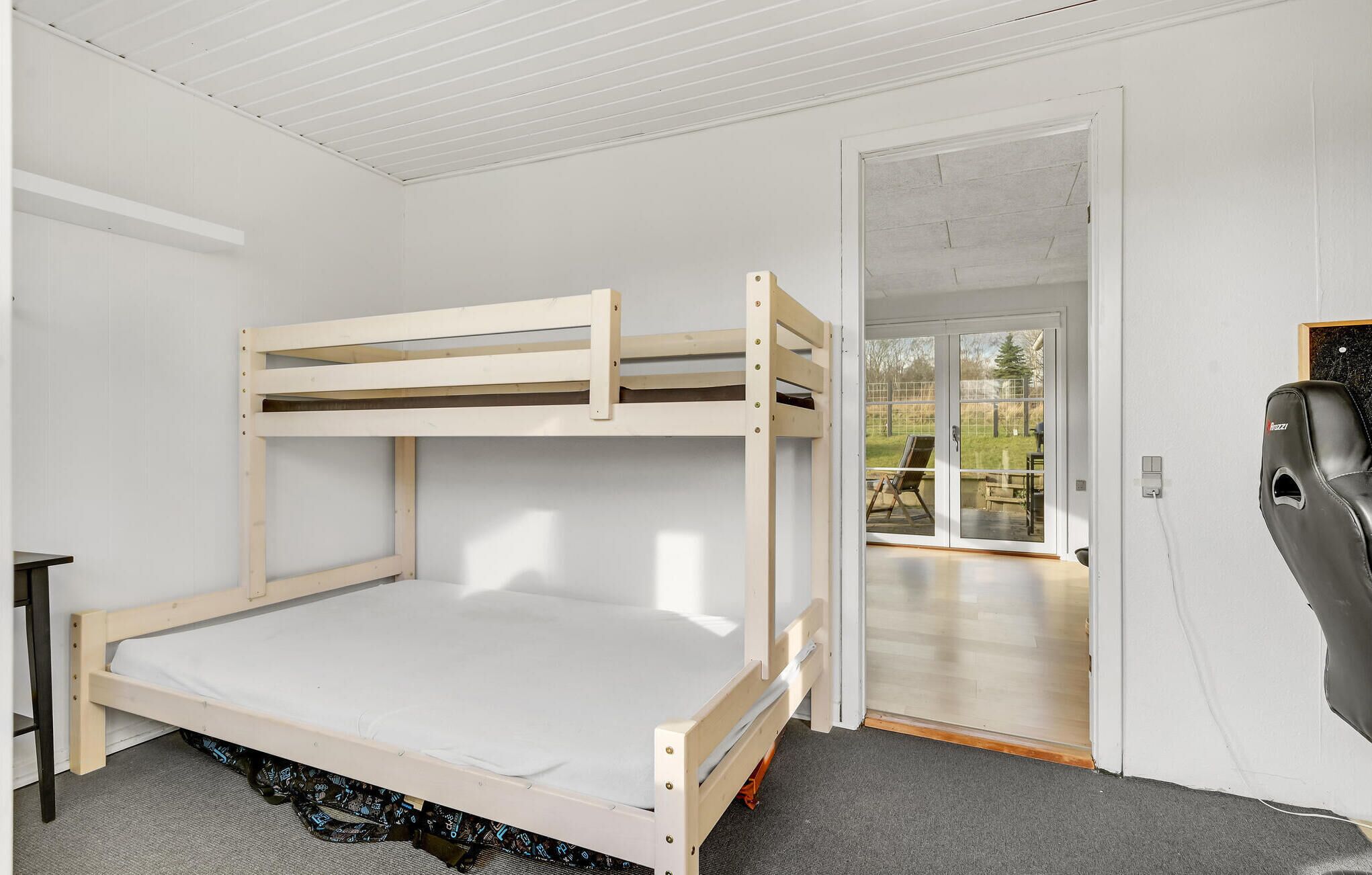 Un lit superposé dans une chambre avec une porte-fenêtre coulissante donnant sur un espace extérieur.