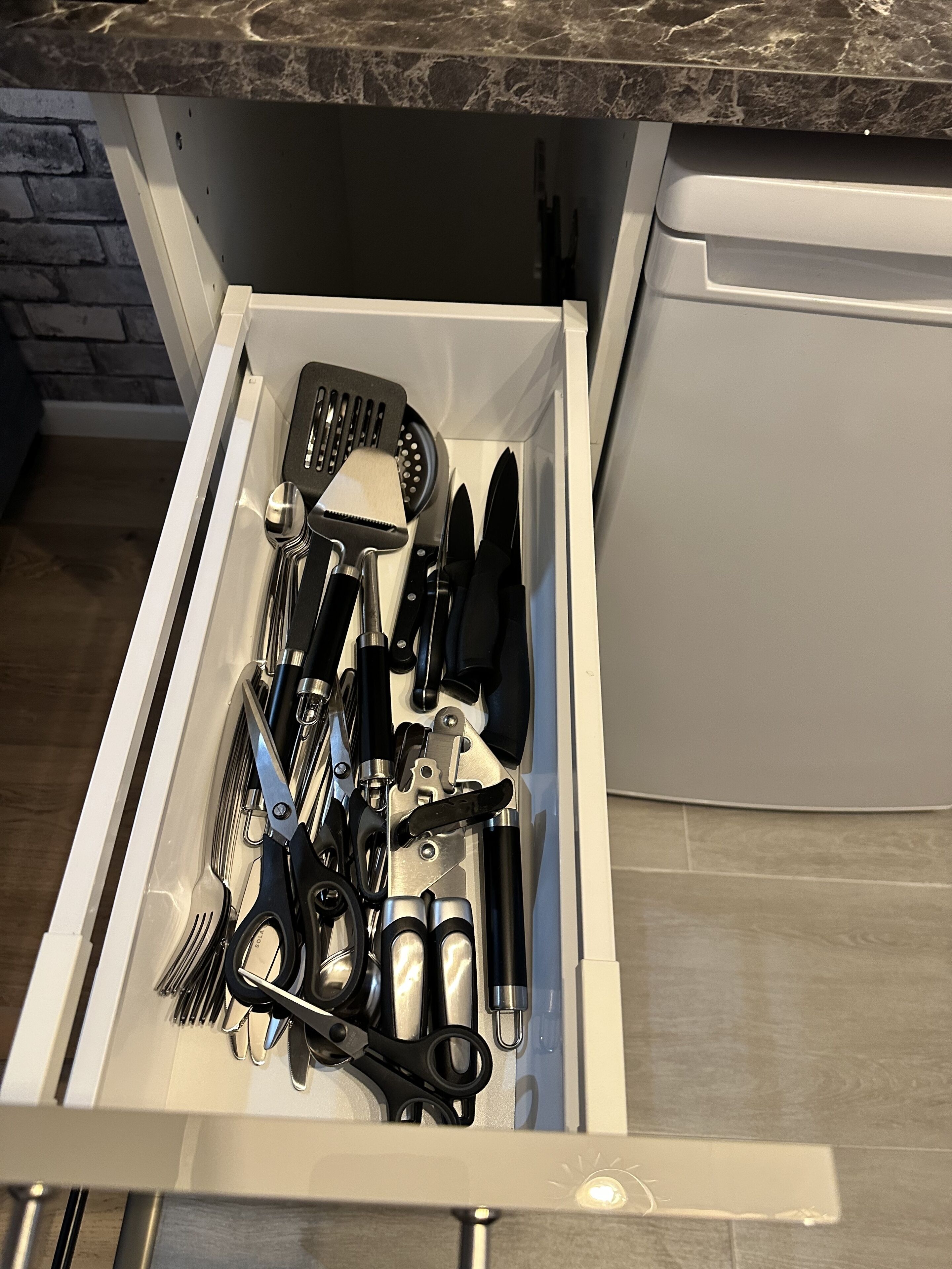 A kitchen drawer with various utensils including a spatula, knife set, and scissors.