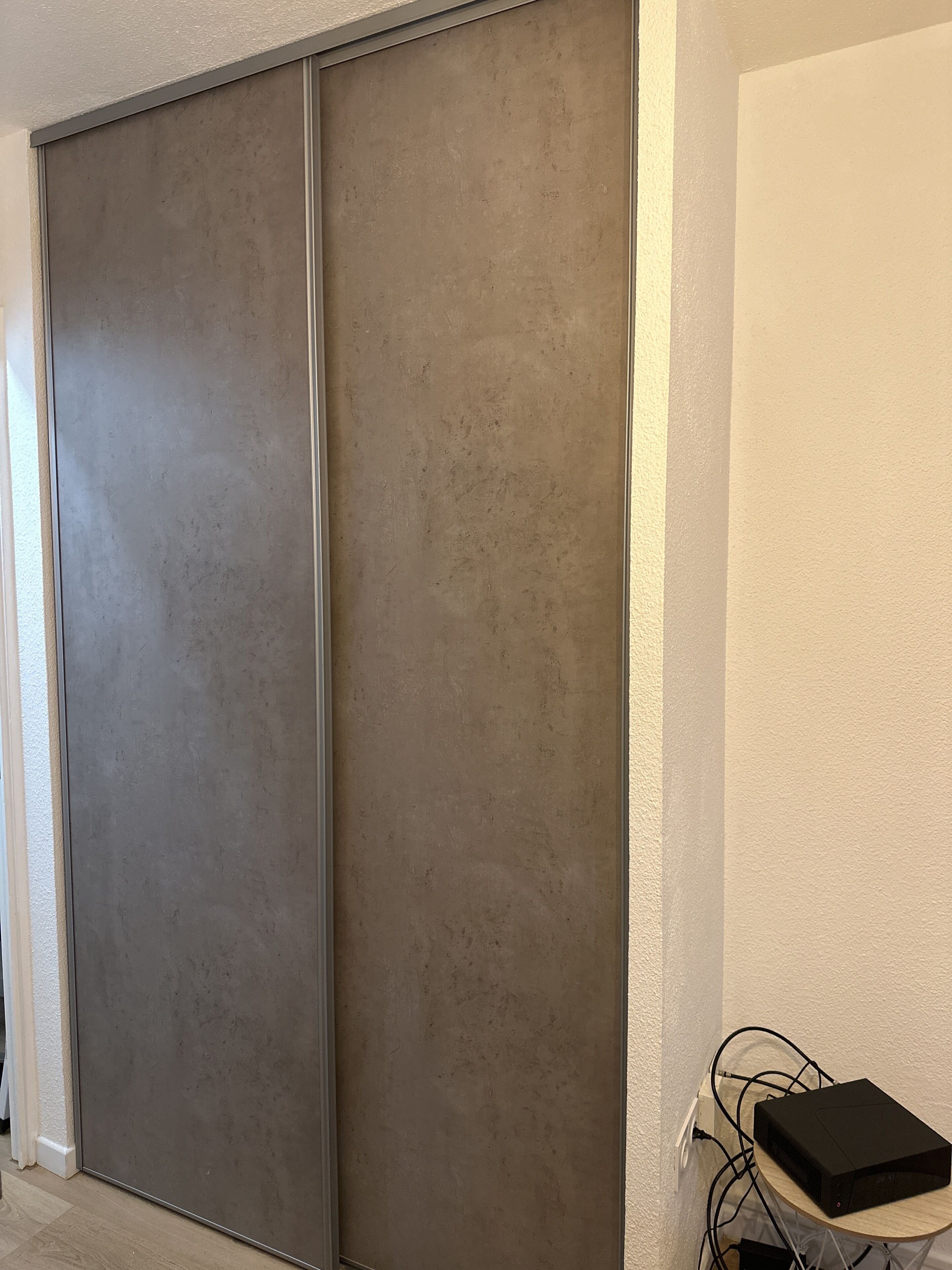 A room with a sliding door, a small table with a black electronic device, and a power outlet.