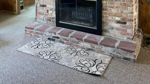 A brick fireplace with a black surround, a decorative shelf with animal figurines, and a patterned rug on the floor.