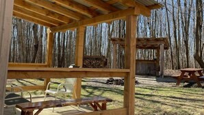 A wooden pavilion with a covered patio area, picnic tables, and a fire pit.
