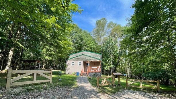 A cabin with a gravel driveway, surrounded by trees, and a wooden fence.