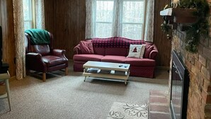 A cozy living room with a wooden ceiling, a red sofa, a leather armchair, and a coffee table.