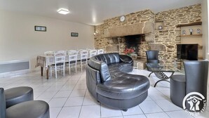 A living room with a stone fireplace, a dining area with white chairs, and a black leather sofa.