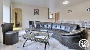 A modern living room with a leather sectional sofa, a glass coffee table, and a dining area with white chairs and a table set for a meal.
