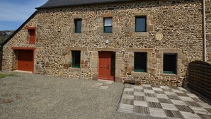 A stone building with multiple doors and windows, a checkered wooden deck, and a gravel driveway.
