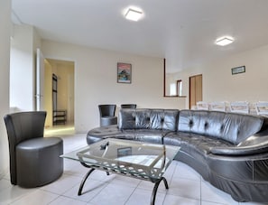 A modern living room with a leather sectional sofa, a glass coffee table, and a dining area with white chairs and a table set for a meal.