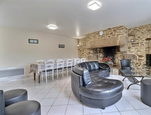 A living room with a stone fireplace, a dining area with white chairs, and a black leather sofa.