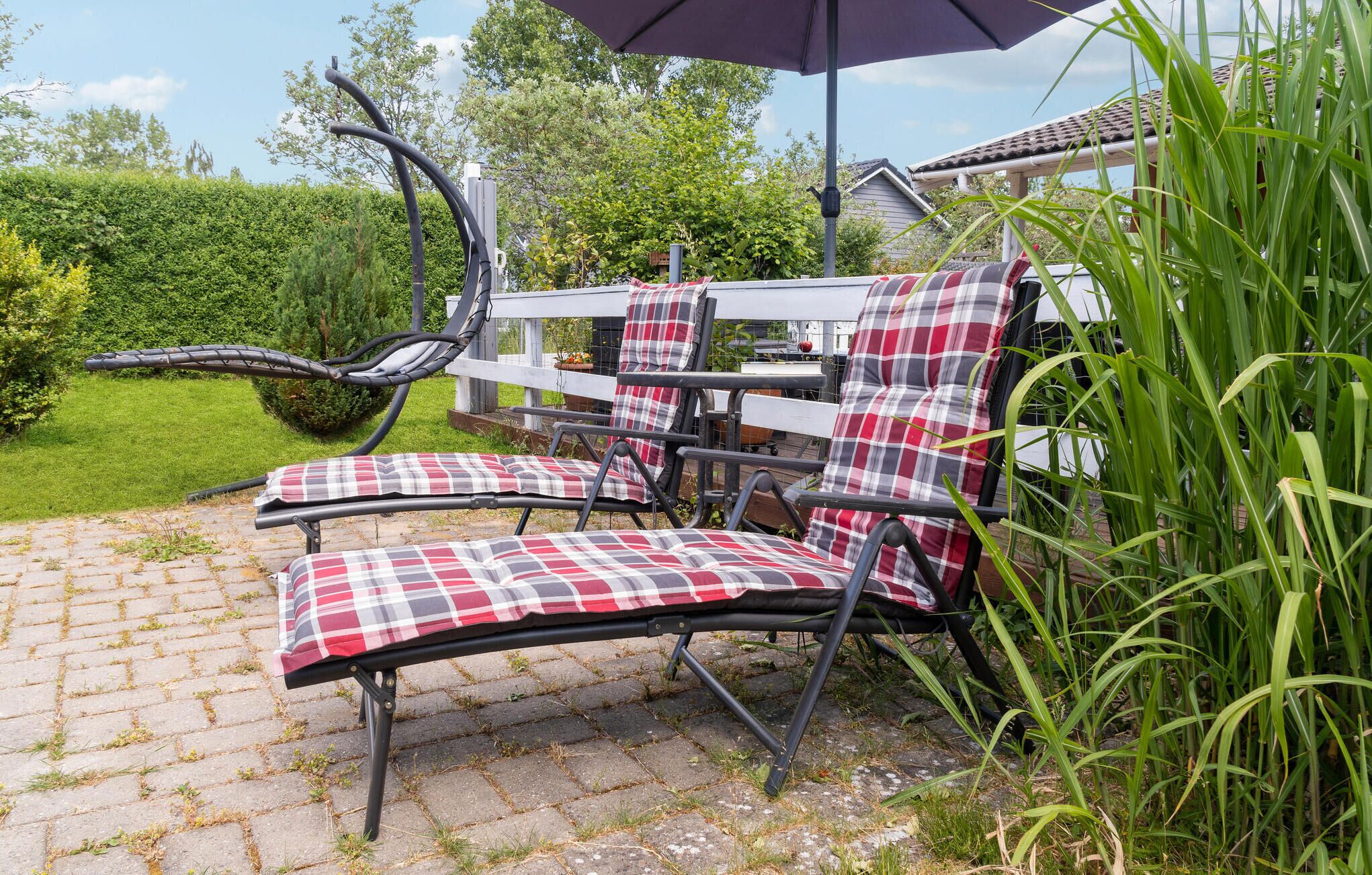 A patio area with a metal table and chairs, a purple umbrella, and a brick pathway.