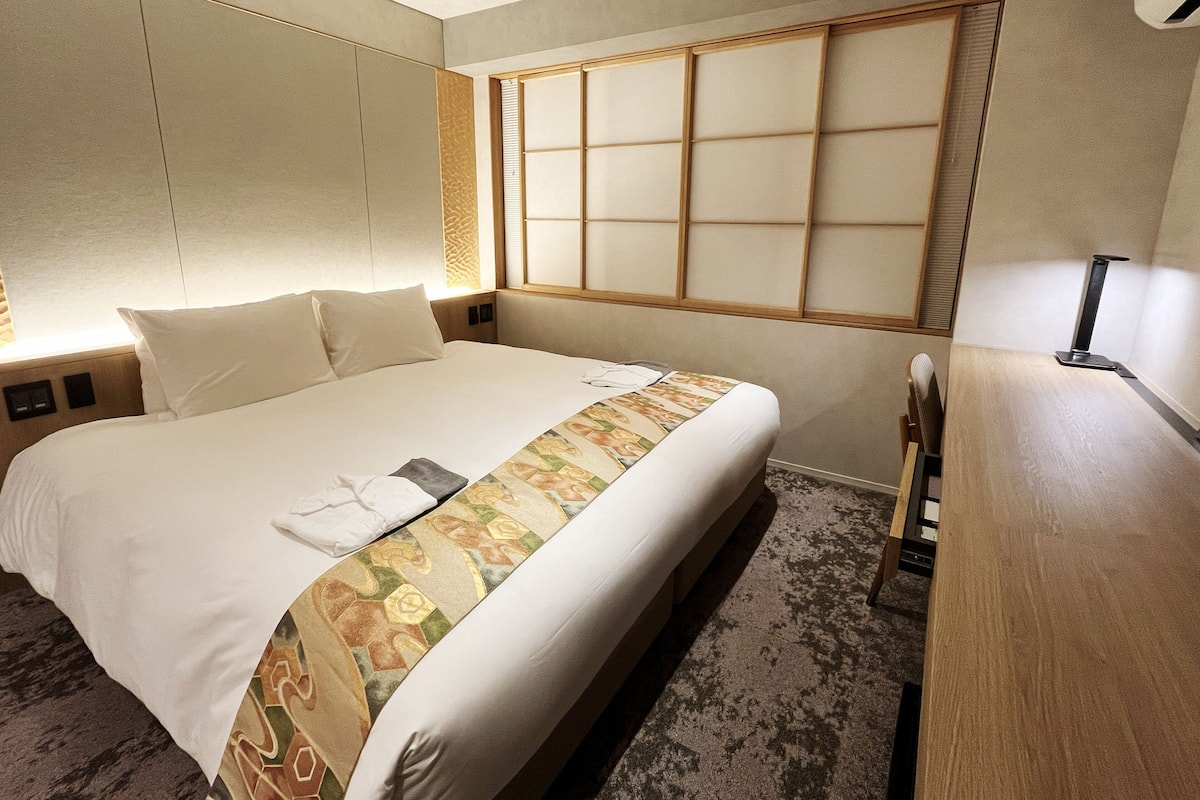 Een hotelkamer met een groot bed, een houten hoofdbord, een nachtkastje en een bureau met een stoel.