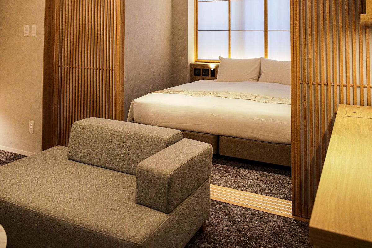 Een hotelkamer met een bed, een bank, een houten wand en een ventilatieopening in het plafond.
