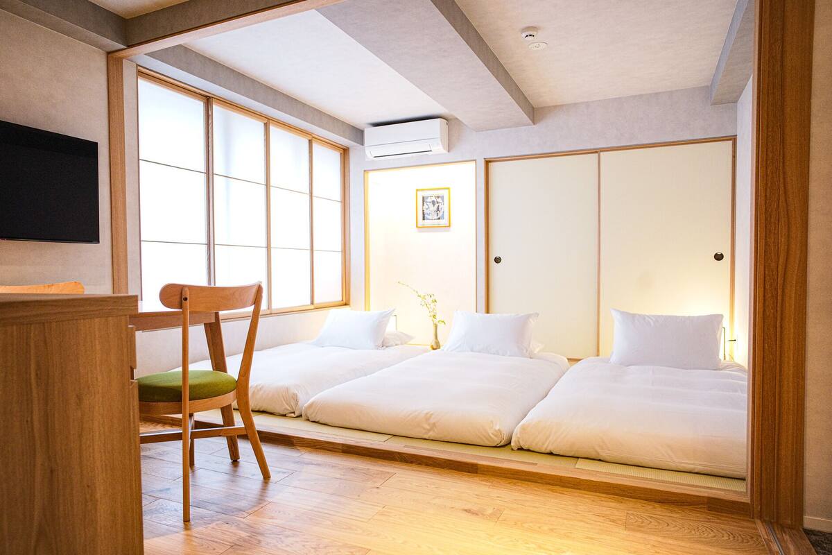 Een traditionele Japanse kamer met tatami vloerbedekking, een laag houten bed, een houten stoel met een groene kussen en een schuifdeur van shoji-schermen.