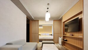 Ein modernes Hotelzimmer mit einer Couch, einem kleinen Tisch, einem Bett, einem Fernseher und einem Holzschrank.