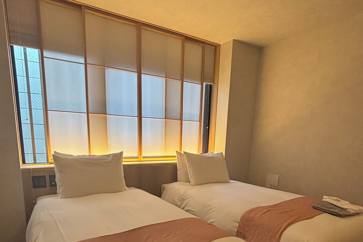 Een hotelkamer met twee bedden, een groot raam met luxaflex en een vloerbedekking.