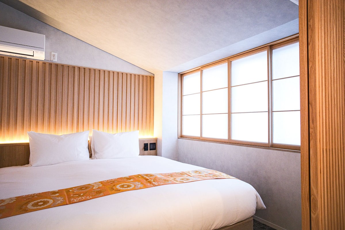 Een hotelkamer met een groot bed, een houten hoofdeinde, een raam met zonwering en een airconditioning op de muur.