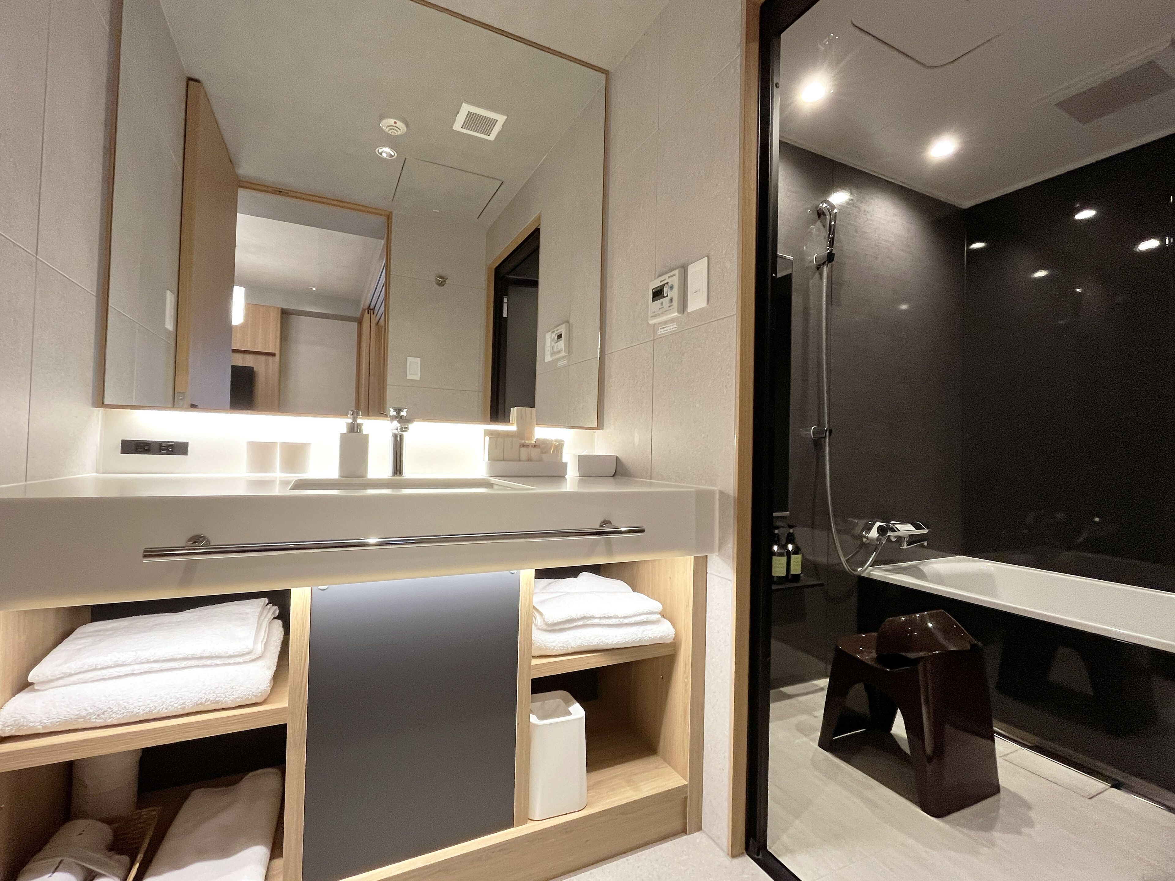 A modern bathroom with a large mirror, a sink, a shower, and a vanity with shelves.