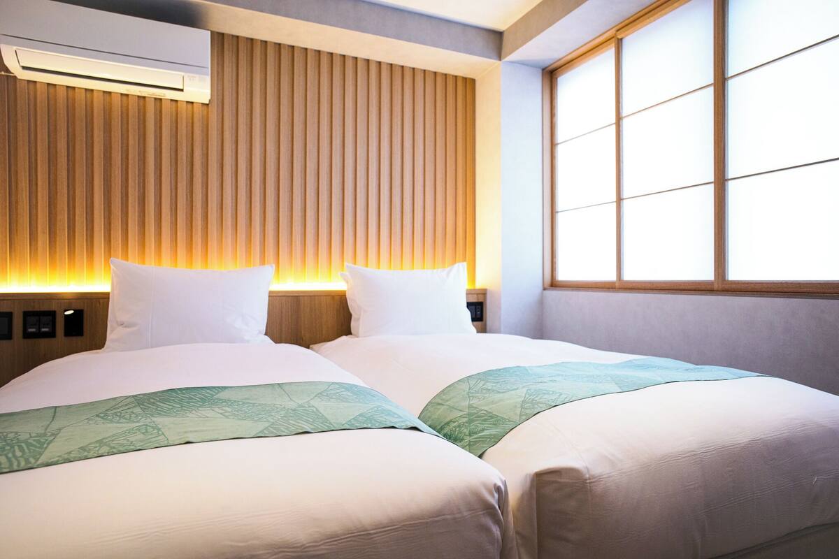 Een hotelkamer met twee bedden, een houten lattenkap, een groot raam en een airconditioning.