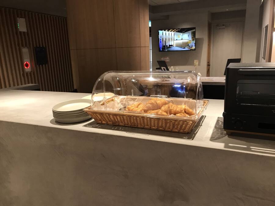 Aamiaistarjoilualue, jossa on rottinkikori täynnä croissantteja, pino lautasia ja kahvinkeitin.