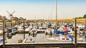 Uma marina com vários barcos atracados, um moinho de vento ao fundo e céu claro.