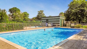 Piscina retangular com borda revestida de azulejos, cercada por uma grade de metal.