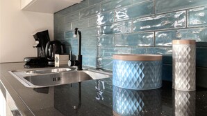 Cozinha moderna com pia de aço inoxidável, máquina de café e um recipiente azul estampado no balcão.
