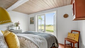 Een slaapkamer met een groot bed, een nachtkastje met een lamp, een stoel en een raam met uitzicht op het landschap.