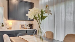Een moderne keuken met donkere kastjes, een koffiezetapparaat en een vaas met witte bloemen op het aanrecht.