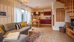 Ein gemütliches Wohnzimmer mit einer Couch, einem kleinen Tisch und einem farbenfrohen Teppich. Es gibt eine Küchenzeile mit Holzschränken und einem Esstisch.