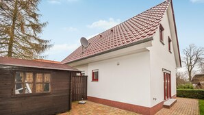 Ein zweistöckiges Haus mit rotem Ziegeldach, einer Sat-Anlage und einem kleinen, umzäunten Bereich mit einer Holzkonstruktion.