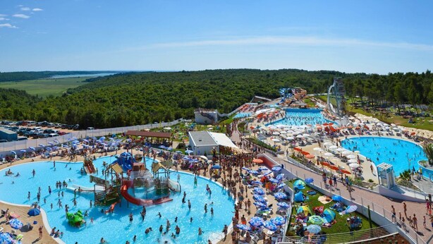 Un grand complexe de piscines extérieures comprenant plusieurs bassins et toboggans aquatiques, entouré de parasols et de chaises de plage.