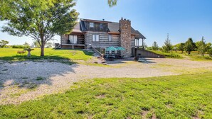 A log cabin with a stone chimney, a covered patio, and a gravel driveway. - Peace & Quiet on Alpaca Farm! Paola Studio (Paola)