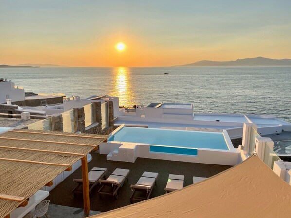 A rooftop pool area with lounge chairs and a view of the sunset over the sea.
