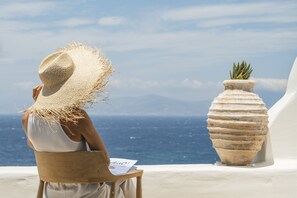 A person sitting on a wooden chair with a straw hat, overlooking the sea.
