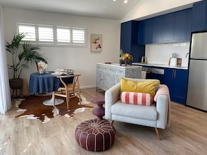 Une cuisine moderne avec des meubles bleus, un coin repas avec une table et des chaises, et un salon avec un canapé et un pouf.