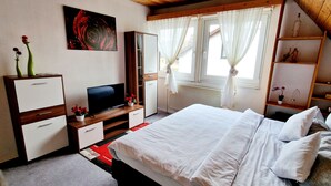 Une chambre à coucher avec un lit, une télévision, une commode et une fenêtre avec des rideaux.