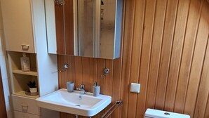 Une petite salle de bain avec un lavabo blanc, un miroir et des toilettes. Les murs sont recouverts de panneaux en bois et un tapis à rayures recouvre le sol.