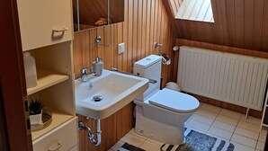 Une petite salle de bain privative avec un intérieur en bois, un puits de lumière, un lavabo blanc, des toilettes et un radiateur.