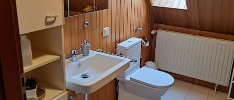 Ein kleines, privates Badezimmer mit Holzvertäfelung, einem Oberlicht, einem weißen Waschbecken, einer Toilette und einem Heizkörper.
